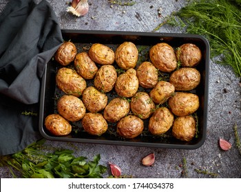 Tasty fresh homemade baked potatoes served on a metal tray. With various herbs, butter, garlic and salt. Gray stone background. View from above.