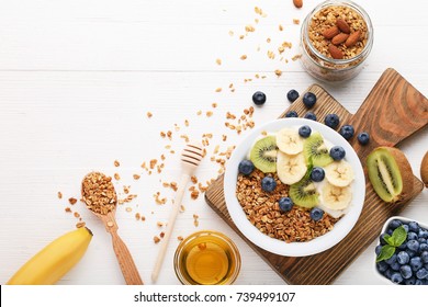 Tasty granola with berries in plate with honey on white wooden table