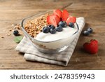 Tasty granola with berries and yogurt in bowl on wooden table, closeup