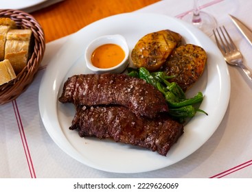 Tasty grilled beef steak marinated in piquant chimmichurri with side dish of unpeeled baked potatoes - Shutterstock ID 2229626069