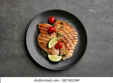 Tasty grilled chicken fillets with tomatoes, lime slices and green sprouts on grey table, top view