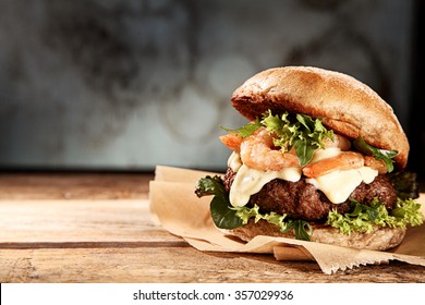 Tasty grilled prawn and beef burger with lettuce and mayonnaise served on pieces of brown paper on a rustic wooden table of counter, with copyspace