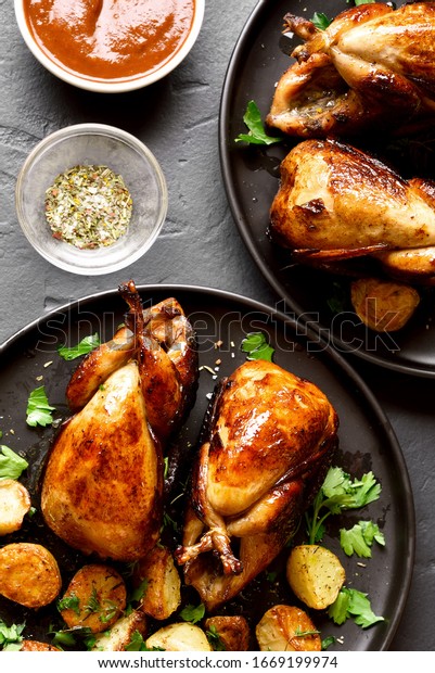 Tasty grilled quails\
carcasses on black stone background. Roasted quails on plate. Top\
view, flat lay