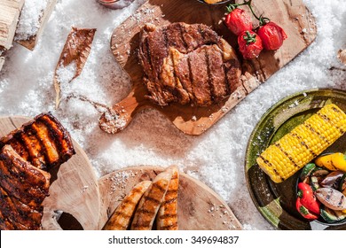 Tasty grilled rib-eye steak, spicy spare ribs and sausages served with corn on the cob outdoors in winter snow