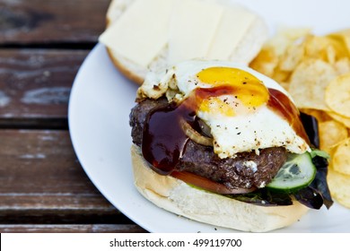 Tasty Hamburger And Crisps With A BBQ Sauce Drizzled Over A Fried Egg.on A Wooden Slatted Table.