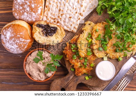 Tasty Hanukkah celebration food: homemade traditional potato, crunchy matzo, liver pate, sweet donuts on vintage cutting board. Rustic wooden background. Top view
