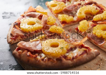 Tasty Hawaiian pizza with pineapple rings and prosciutto ham on a crispy oven-fired base served in portions on a wooden board in close up