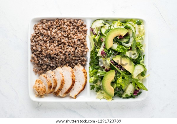 Tasty healthy food. Boiled buckwheat with\
grilled chicken amnd fresh green salad on rectangle plate. Loosing\
weight concept.