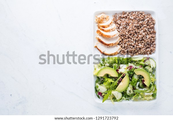 Tasty healthy food. Boiled buckwheat with\
grilled chicken amnd fresh green salad on rectangle plate. Loosing\
weight concept.