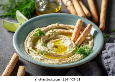 Tasty and homemade hummus with breadsticks, olive oil and dill. Hummus served with breadsticks and olive oil.