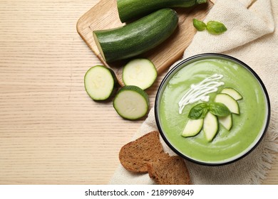 Tasty homemade zucchini cream soup served on wooden table, flat lay