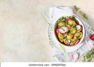 Tasty hot potato salad with green beans, fresh radishes and herbs dressing with olive oil and mustard sauce, light concrete background. Top view. Copy space.