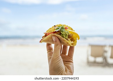 Tasty juicy taco in woman's hand in front of the beach in Tulum, Mexico