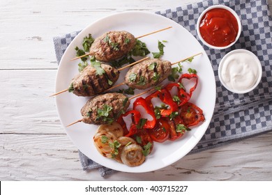 Tasty kofta kebab with grilled vegetables on a plate and sauce on the table. Horizontal view from above
