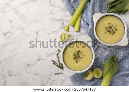 Tasty leek soup in bowls on white marble table, flat lay. Space for text