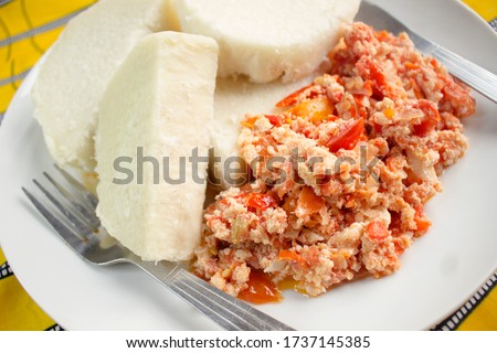 A tasty meal of boiled yam and fried scrambled eggs prepared with sliced onions, tomatoes and red pepper. Ready to eat and served in a white plate with a knife and fork - Close up view