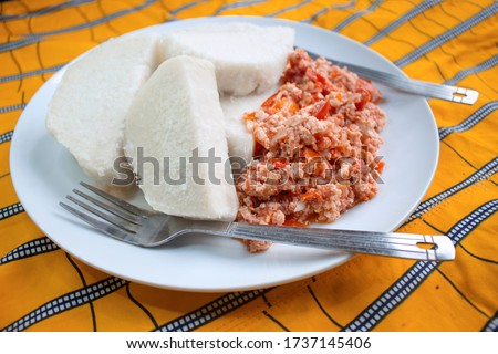 A tasty meal of boiled yam and fried scrambled eggs prepared with sliced onions, tomatoes and red pepper. Ready to eat and served on a colorful orange African pattern tablecloth with a knife and fork 
