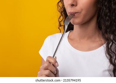 Tasty Meal. Close up of hungry young lady holding fork in her mouth, biting and dreaming about delicious healthy food, choosing something to eat isolated on yellow orange studio wall, free copy space