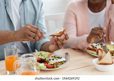 Tasty Meal. Closeup Shot Of Unrecognizable Black Man And Woman Eating Breakfast, African American Couple Enjoying Delicious Food, Sitting At Table In Kitchen, Man Spreading Butter On Bread, Cropped - Powered by Shutterstock