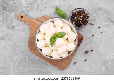 Tasty mozzarella balls and basil leaves in bowl on grey table, flat lay