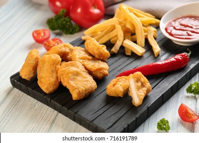 Tasty nuggets, french fries and small bowl with sauce for chicken on wooden board