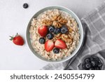 Tasty oatmeal with strawberries, blueberries and walnuts in bowl on grey table, flat lay