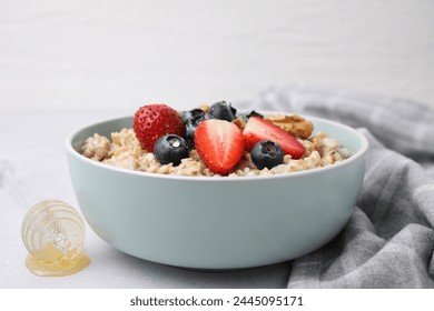 Tasty oatmeal with strawberries, blueberries and walnuts in bowl on grey table
