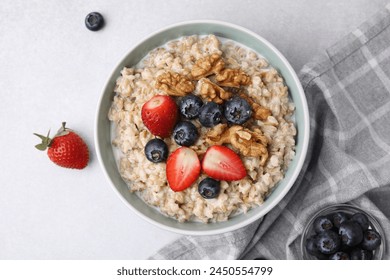 Tasty oatmeal with strawberries, blueberries and walnuts in bowl on grey table, flat lay