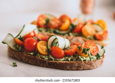 Tasty Open Sandwich From Toasted Sourdough Bread With Mashed Avocado, Slices Of Fresh Cucumber And Cherry Tomatoes