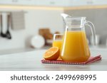 Tasty orange juice in jug, glass and citrus fruit on white marble table. Space for text