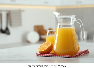 Tasty orange juice in jug, glass and citrus fruit on white marble table. Space for text