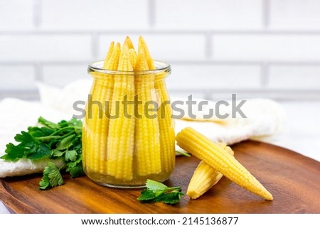Tasty organic yellow sweet pickled small corn cobs canned in a glass jar in the kitchen