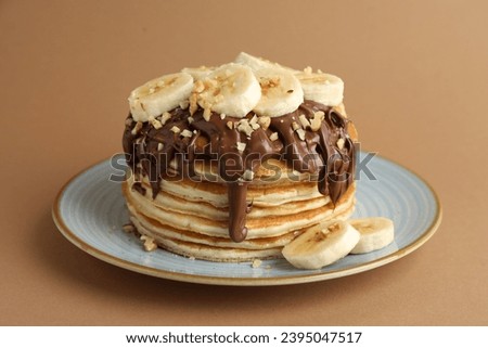 Tasty pancakes with chocolate spread, sliced banana and nuts on brown background, closeup