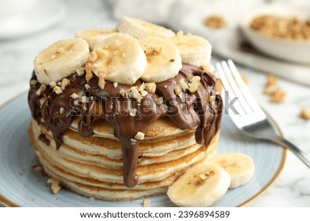 Tasty pancakes with chocolate spread, sliced banana and nuts served on table, closeup