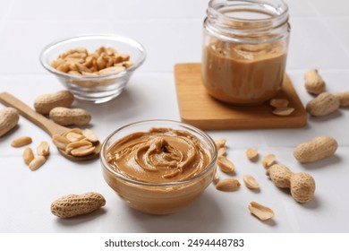 Tasty peanut butter in bowl and groundnuts on white tiled table - Powered by Shutterstock