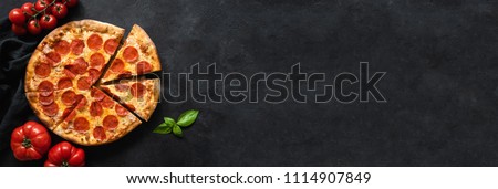 Tasty pepperoni pizza and cooking ingredients tomatoes basil on black concrete background. Top view of hot pepperoni pizza. Banner