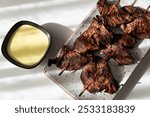 Tasty Peruvian anticuchos on a white background with a portion of hot sauce and illuminated with natural light.