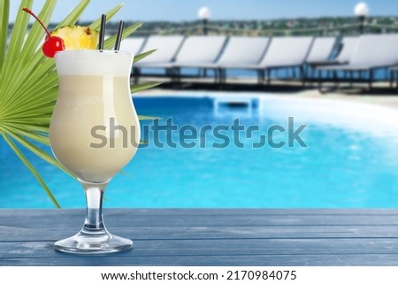 Tasty Pina Colada cocktail on blue wooden table near outdoor swimming pool, space for text