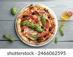 Tasty pizza with cured ham, olives, sun-dried tomato and basil on gray wooden table, top view