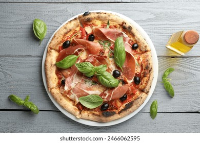 Tasty pizza with cured ham, olives, sun-dried tomato and basil on gray wooden table, top view