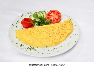 Tasty plain omelet in a plate, next to tomato cucumber and parsley, isolated on white background