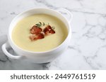 Tasty potato soup with bacon and rosemary in bowl on white marble table, closeup. Space for text