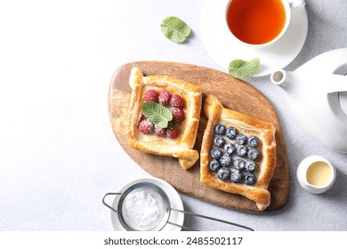 Tasty puff pastries with berries and tea on white table, flat lay. Space for text - Powered by Shutterstock