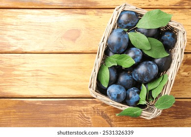 Tasty ripe plums and leaves in wicker basket on wooden table, top view. Space for text - Powered by Shutterstock