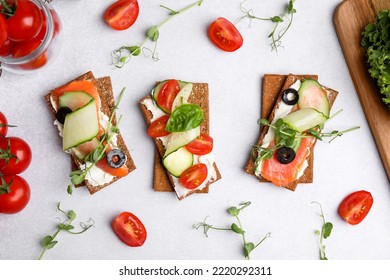 Panecillos de centeno deliciosos con salmón, queso crema y verduras sobre mesa gris claro, lao plano