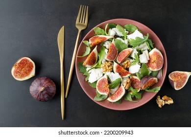 Tasty salad with sliced figs, crushed soft goat cheese, walnut and fresh arugula leaves on red plate on dark  brown background.  - Powered by Shutterstock