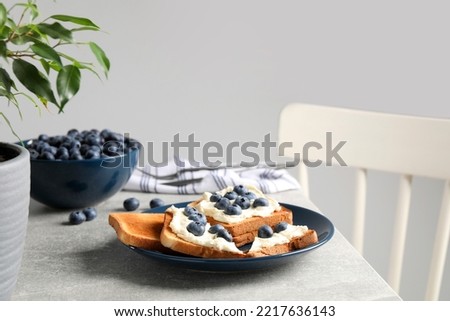 Tasty sandwiches with cream cheese and blueberries on grey table indoors