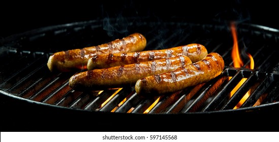 Tasty Sausages Sizzling On A Portable BBQ Fire Grilling Over The Flames On A Summer Picnic, Close Up View