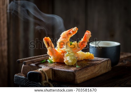 Tasty shrimp in tempura with red sauce on black background