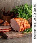 Tasty smoked pork ham with rosemary, onion, garlic, red pepper, and bay leaves. Smoked meat on a kitchen table.